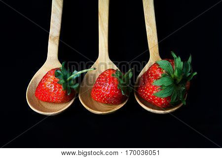 strawberry in wooden spoon on black background isolated