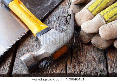 A close up image of an old hammer and work gloves on a wooden workbench.