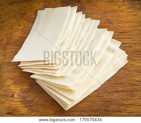 Heap of Uncooked Lasagna Sheets or Dry Italian Pasta on Old Wooden Cutting Board