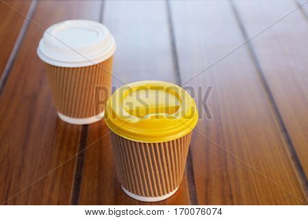 Two paper cups with tasty hot coffee on wooden table, close up view