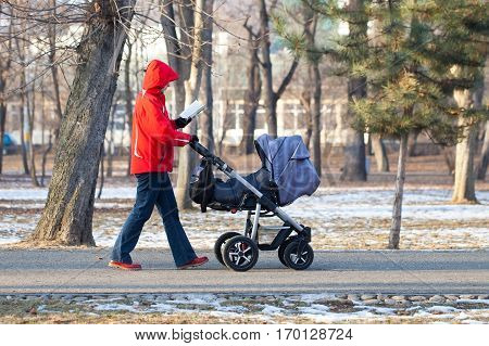 Picture of a mother walking her baby and reading in the park