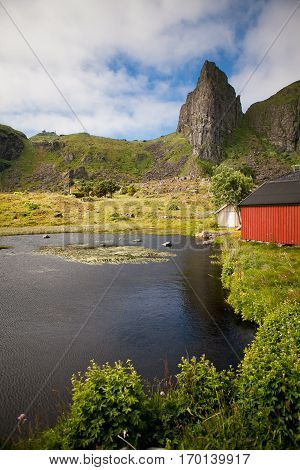 Summer Norwegian Landscape with a pond, red cabin in a meadow and a mountain