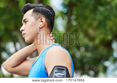 Head and shoulders portrait of serious Vietnamese athlete holding hand on aching neck while having short break during training, profile view