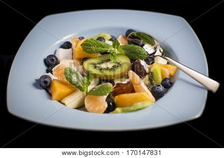 Delicious tasty exotic fruit salad in a blue plate with a spoon