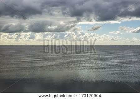 shoreline of Ameland Island with view over the wadden sea with clouds and tourmented sky reflecting in water at dawn