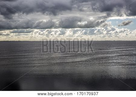 shoreline of Ameland Island with view over the wadden sea with clouds and tourmented sky reflecting in water at dawn