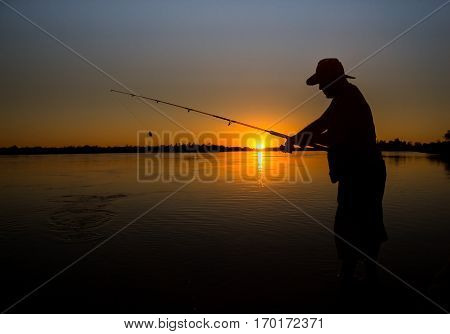 Young man fishing on a river from the boat at sunset silhouette