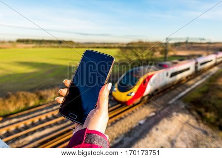 Day View Of Woman Hand Holding Smartphone Over Uk Railroad.