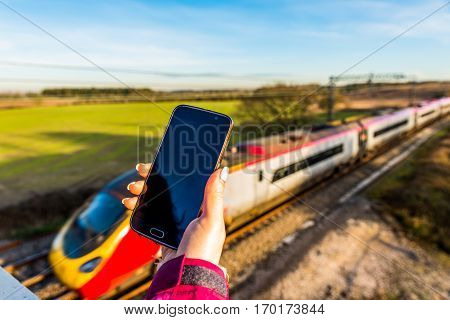 Day View Of Woman Hand Holding Smartphone Over Uk Railroad.