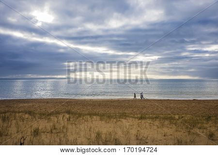group of people wandering on the beach at sunset by a cloudy winter day