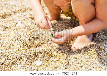 Little boy collects pebbles on the beach