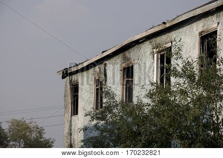 Burnеd light blue two-storeyed building with green trees. After fire