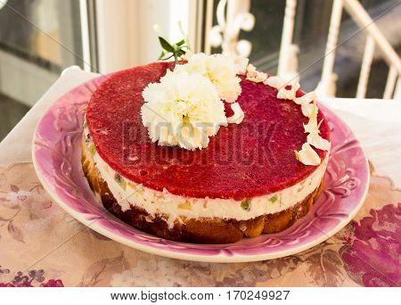 Closeup of a strawberry cake from side on white batskground sponge cake with jelly and fruit on the background of the railing. decorated with white flowers