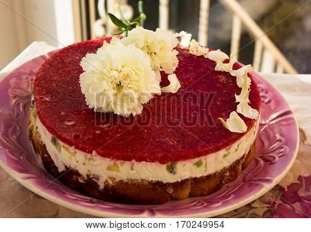 Closeup of a strawberry cake from side on white batskground sponge cake with jelly and fruit on the background of the railing. decorated with white flowers