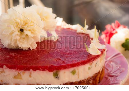 Closeup of a strawberry cake from side on white batskground sponge cake with jelly and fruit on the background of the railing. decorated with white flowers