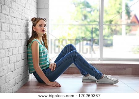Sad teenage girl sitting near window in a room