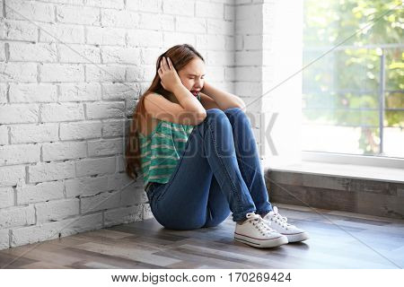 Sad teenage girl sitting near window in a room