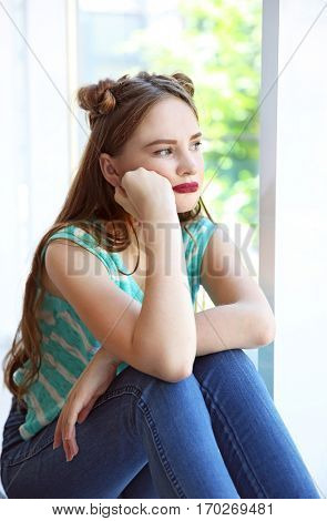 Sad teenage girl sitting near window