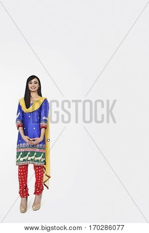Full length portrait of Indian woman in traditional wear standing over gray background