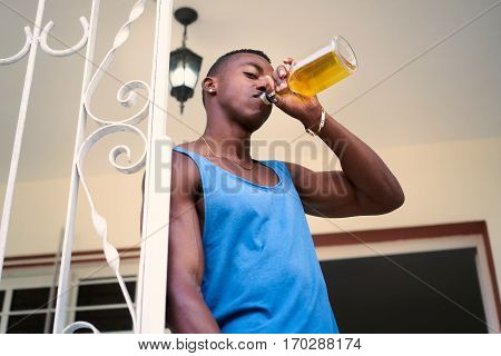 Social issues and substance abuse. Alcoholic young black man drinking alchool from liquor bottle at home looking at camera