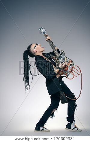 Stylish expressive rock musician is playing electrical guitar and shaking his hair. Full length studio shot. Entertainment and musical concept. 