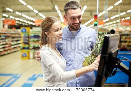 shopping, food, sale, consumerism and people concept - happy couple buying pineapple at grocery store or supermarket self-service cash register