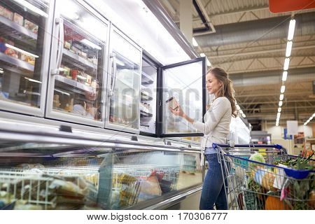 sale, food, consumerism and people concept - woman with shopping cart choosing ice cream at grocery store freezer