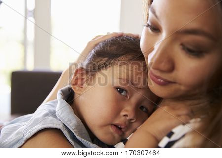 Mother Cuddling Daughter On Sofa At Home