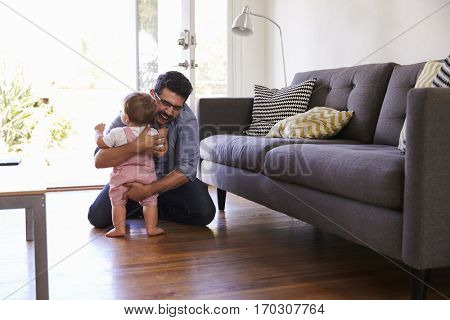 Father Watching Baby Daughter Take First Steps At Home