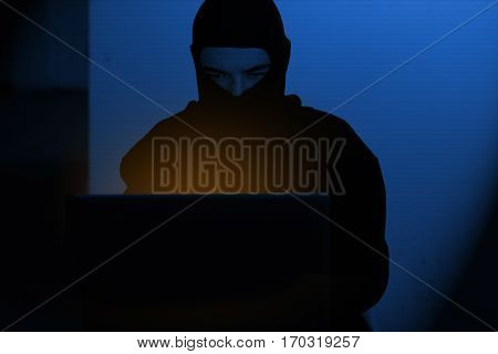 Hacker man in hoodie shirt typing hacking global netwok security on computer laptop over dark background with blue light