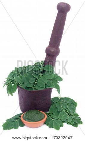 Edible moringa leaves in a vintage mortar with ground paste over white background