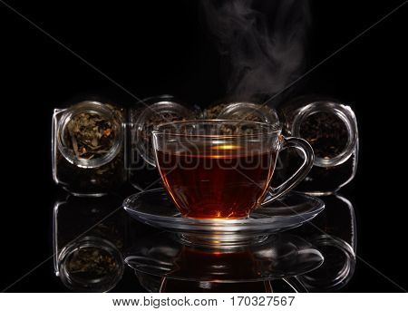 Various kinds of dry tea in glass jars and cup of aromatic tea standing on a black background.  Different kinds of tea leaves.
