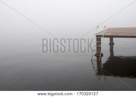 A wooden pier and stairs to sea in a foggy day.