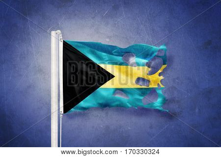 Torn flag of Bahamas flying against grunge background.