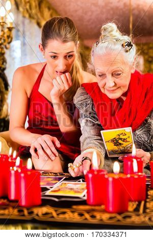 Fortuneteller laying Tarot cards with client on pentagram, candles are burning