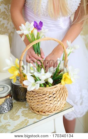 Woman in white dress takes flower from basket on table in studio, noface