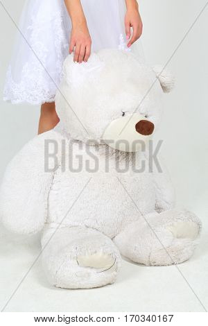 Woman in white dress stands with big toy bear in white studio, noface
