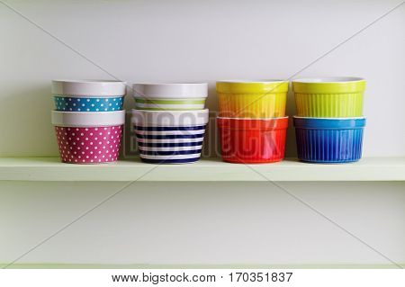Colorful bowls on a kitchen shelf. A kitchen shelf unit holding striped and spotted bowls. Kitchen shelf arrangement. 