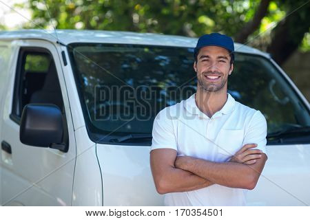 Portrait of cheerful delivery man with arms crossed while standing by van