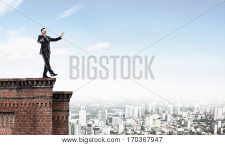 Businessman with blindfolder on eyes walking on building top