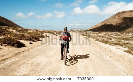 a young caucasian man seen from behind riding a bike in a dirty road in La Graciosa, Canary Islands, Spain