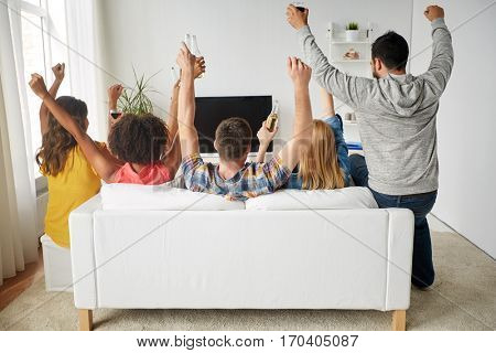 friendship, holidays and people concept - happy friends with beer sitting on sofa and watching tv at home