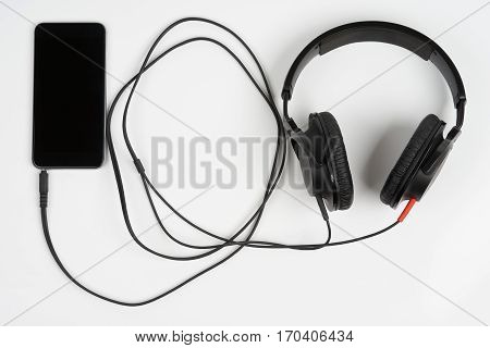 Closed back stereo headphones connected to smart phone on white background
