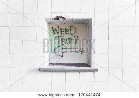 Graffiti words WEED TRIP in a window on a white tiles wall