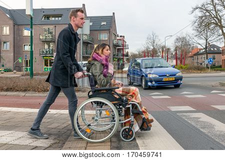 SOEST THE NETHERLANDS - JAN 28: Man pushing a woman in a wheelchair at a zebra crosssing in a Dutch village on Januari 28 in Soest the Netherlands