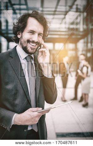 Portrait of businessman with digital tablet talking on mobile phone in office premises