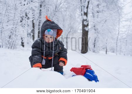 Children's winter games outdoors. The image of a child plays with snow in winter park. and playing with a large colourful toy car. Little Baby Playing with Snow in Winter Outdoors