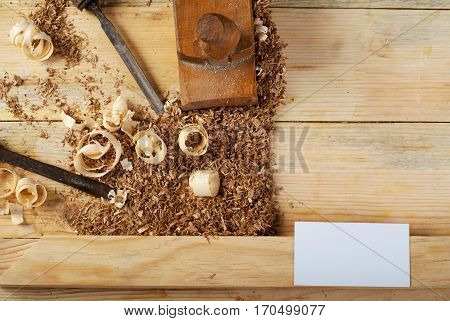 Blank business card on wooden table for carpenter tools with sawdust top view.