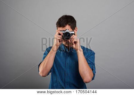Attractive man keep photo with grey background. Tourism concept. Guy use vintage camera. Hipster photographer in blue shirt in studio.