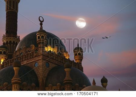 The plane flies against the backdrop of the moon Al Sahaba Mosque.